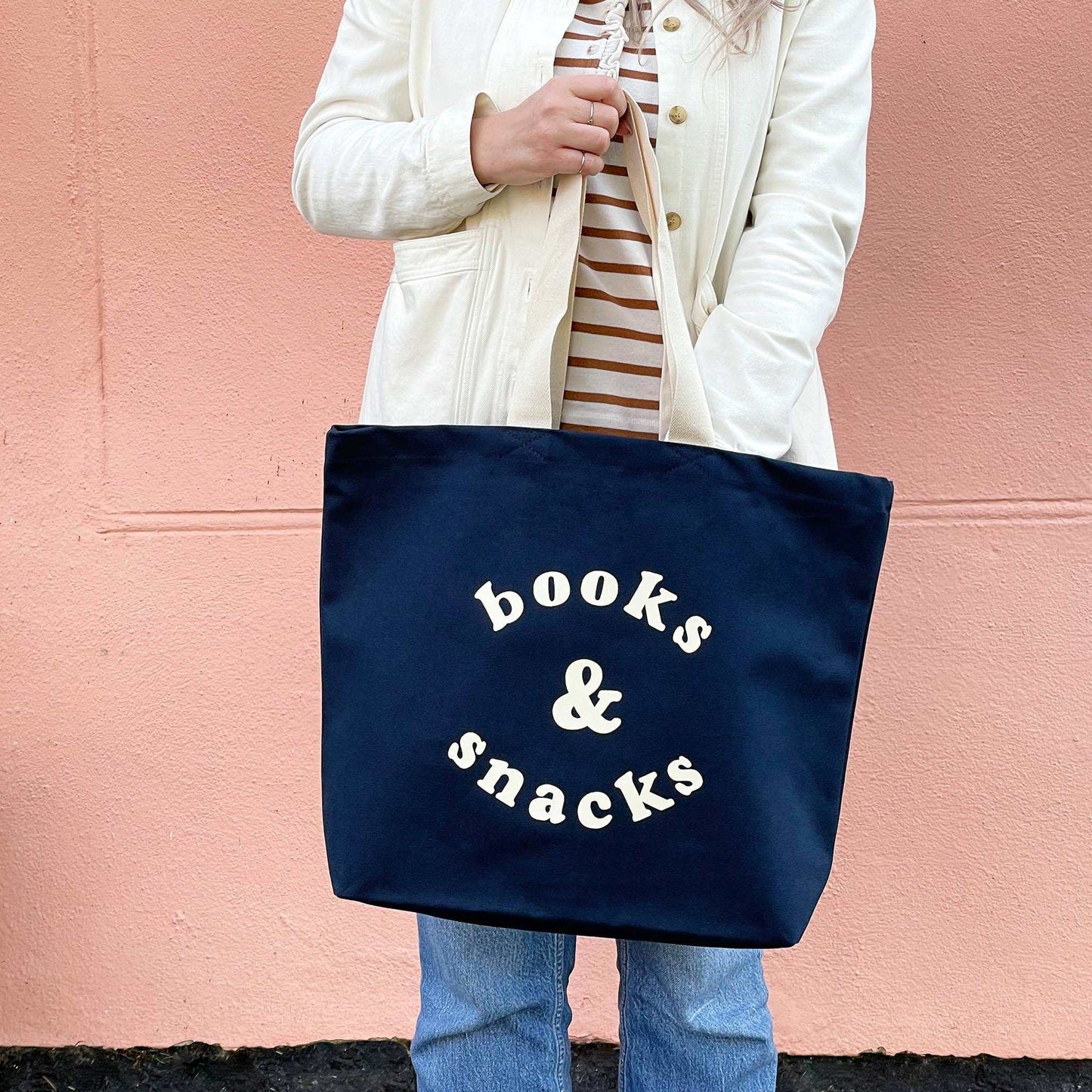 Midnight blue canvas tote bag with "Books & Snacks" design in off-white.