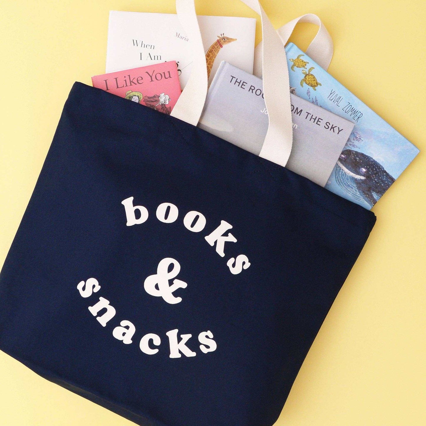 Midnight blue canvas tote bag with 'Books & Snacks' text and books peeking out.