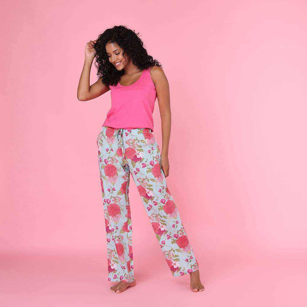 Woman wearing floral Cassie Pant in a bag, pink top, standing against a pink background.