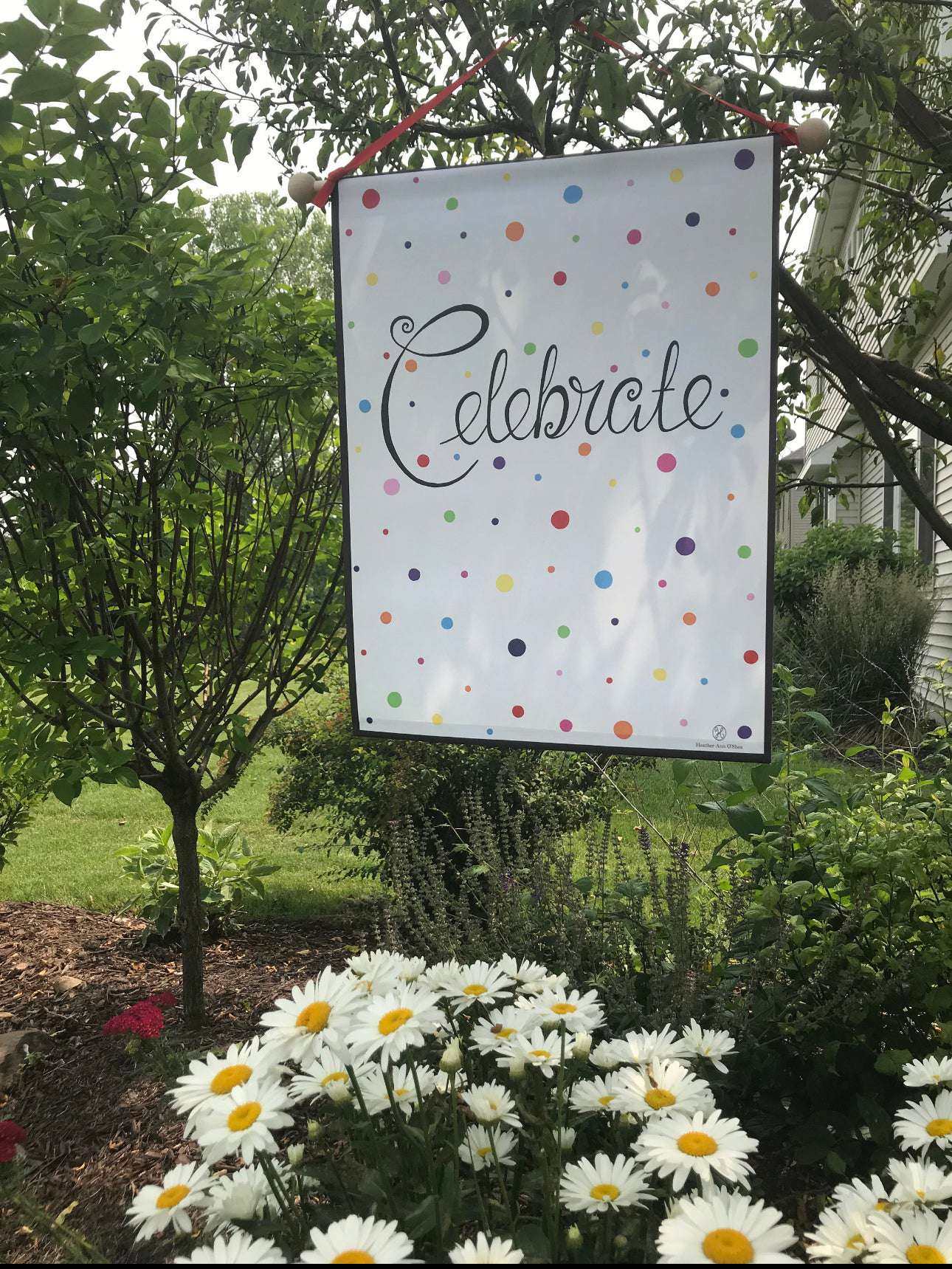 Celebrate Banner in rainbow colors hanging outdoors among greenery, highlighting cheerful and versatile design.