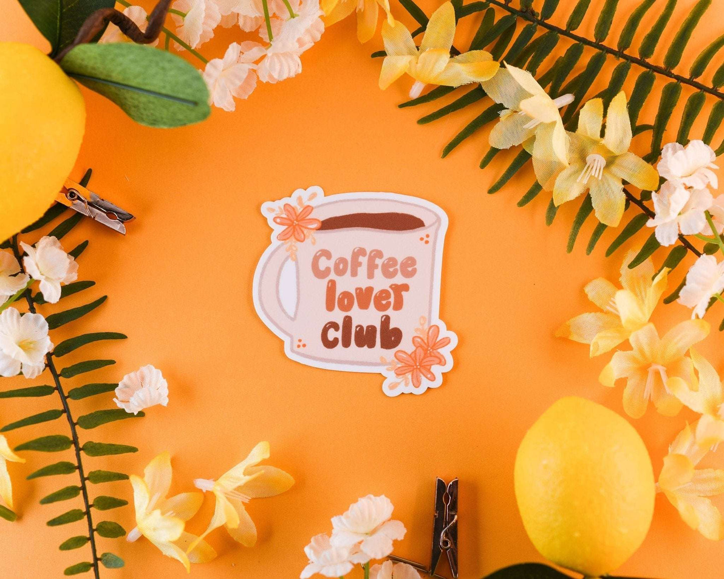Coffee sticker featuring a mug with "Coffee lover club" text, surrounded by flowers on an orange background.
