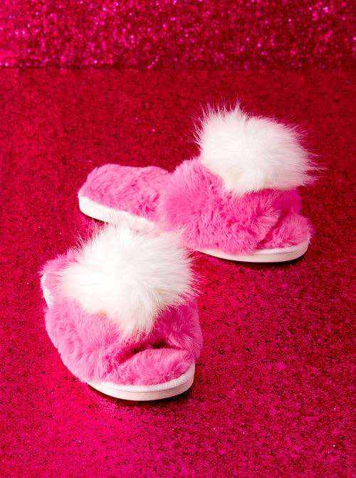 Cozy Pink Amor Slippers with fluffy pom detail on a pink background.