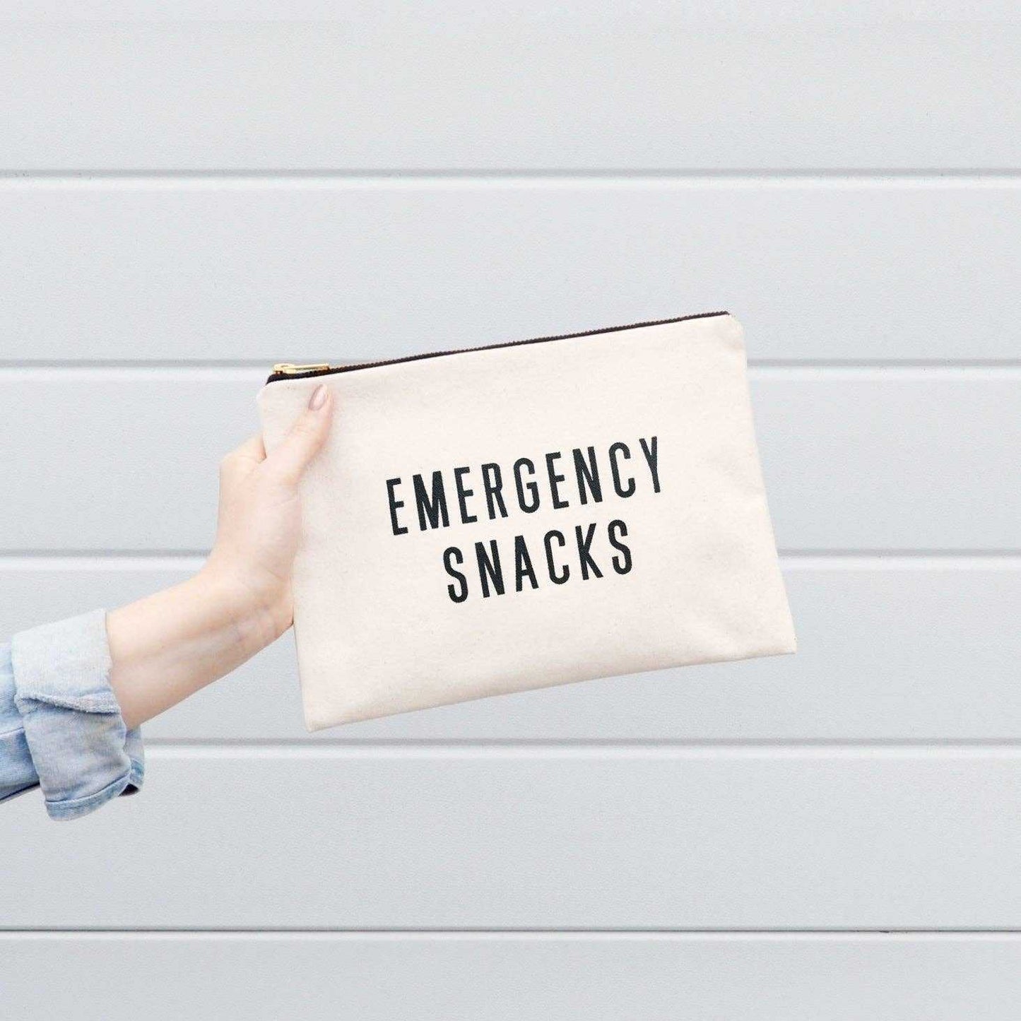 Emergency Snacks large canvas pouch with black print, gold zip, held by a person.