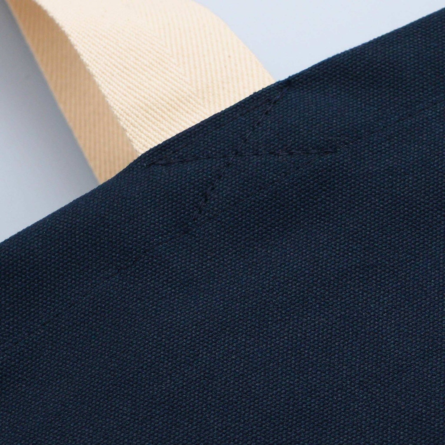 Midnight blue canvas tote bag corner with cream handle detail.