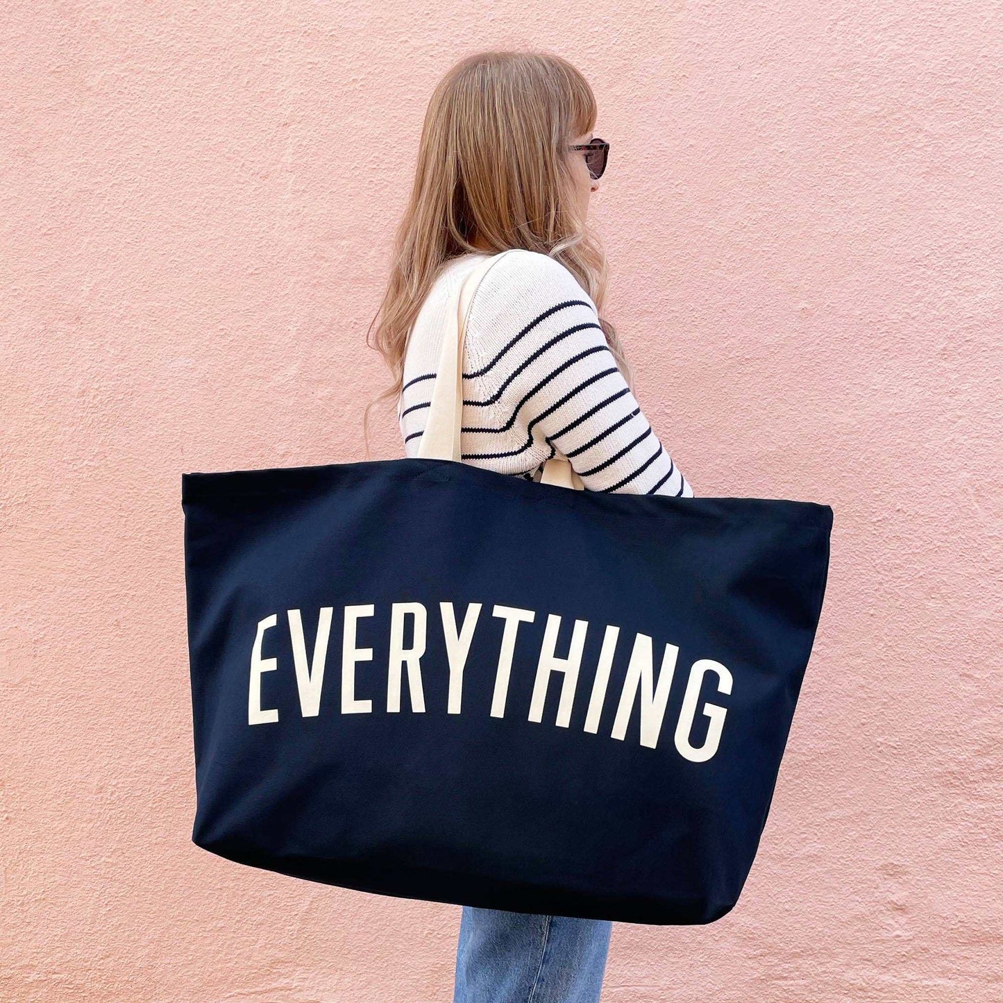Midnight blue REALLY big canvas tote bag with "Everything" printed, held by person against peach wall.