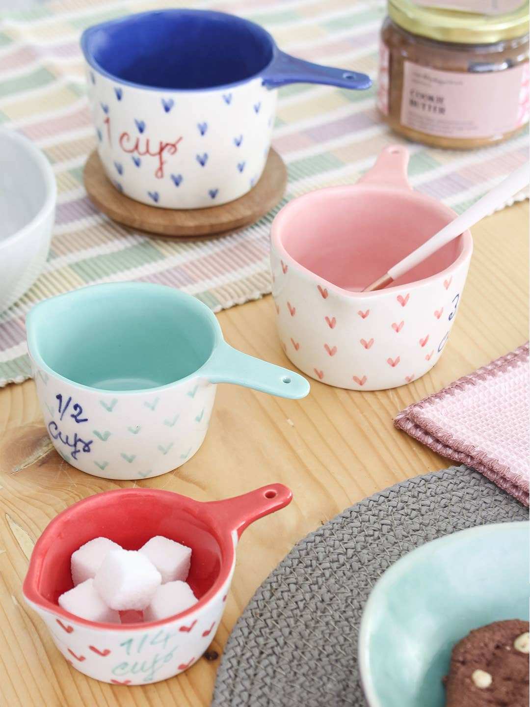 Set of four handpainted ceramic measuring cups with little hearts design on a wooden table.