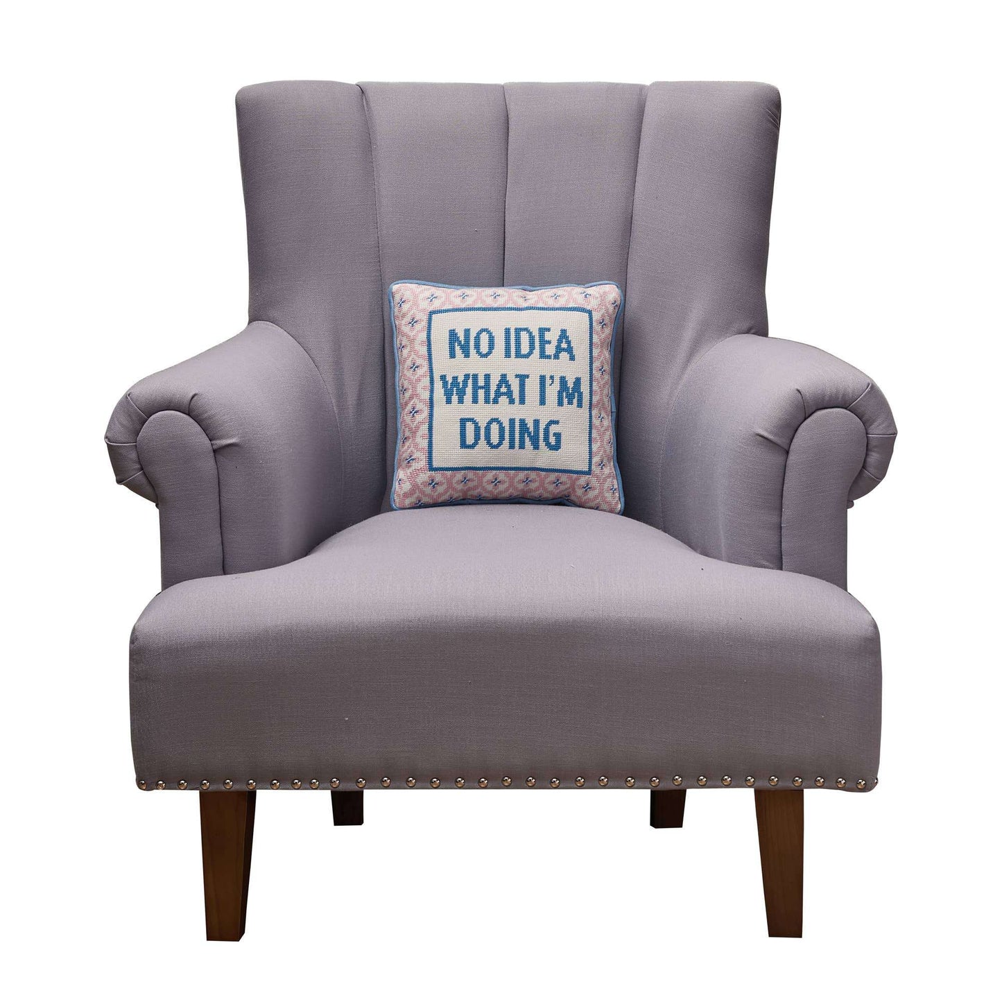 Embroidered needlepoint pillow with "No Idea What I'm Doing" text on a gray armchair.