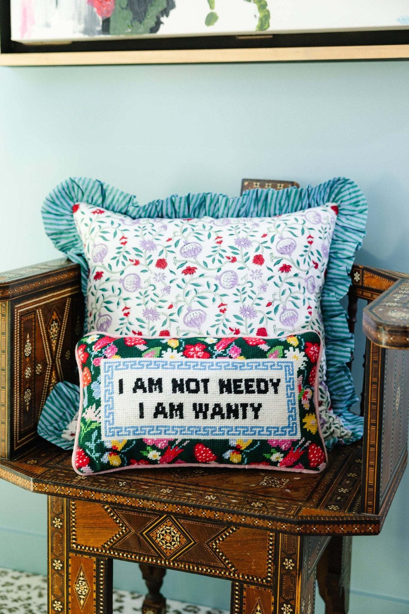 Not Needy Needlepoint Pillow with embroidered message and pink velvet backing on chair.