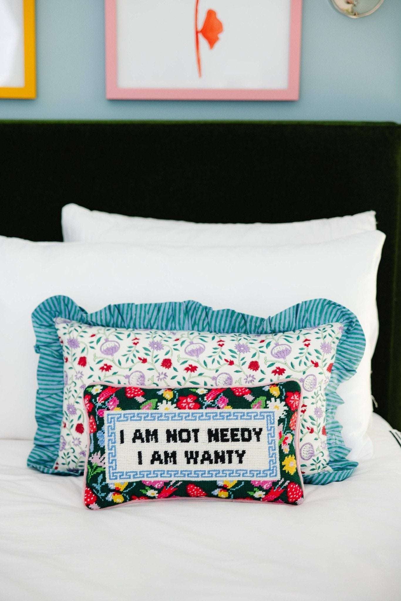 Colorful decorative pillow with slogan "I Am Not Needy, I Am Wanty" on a bed.