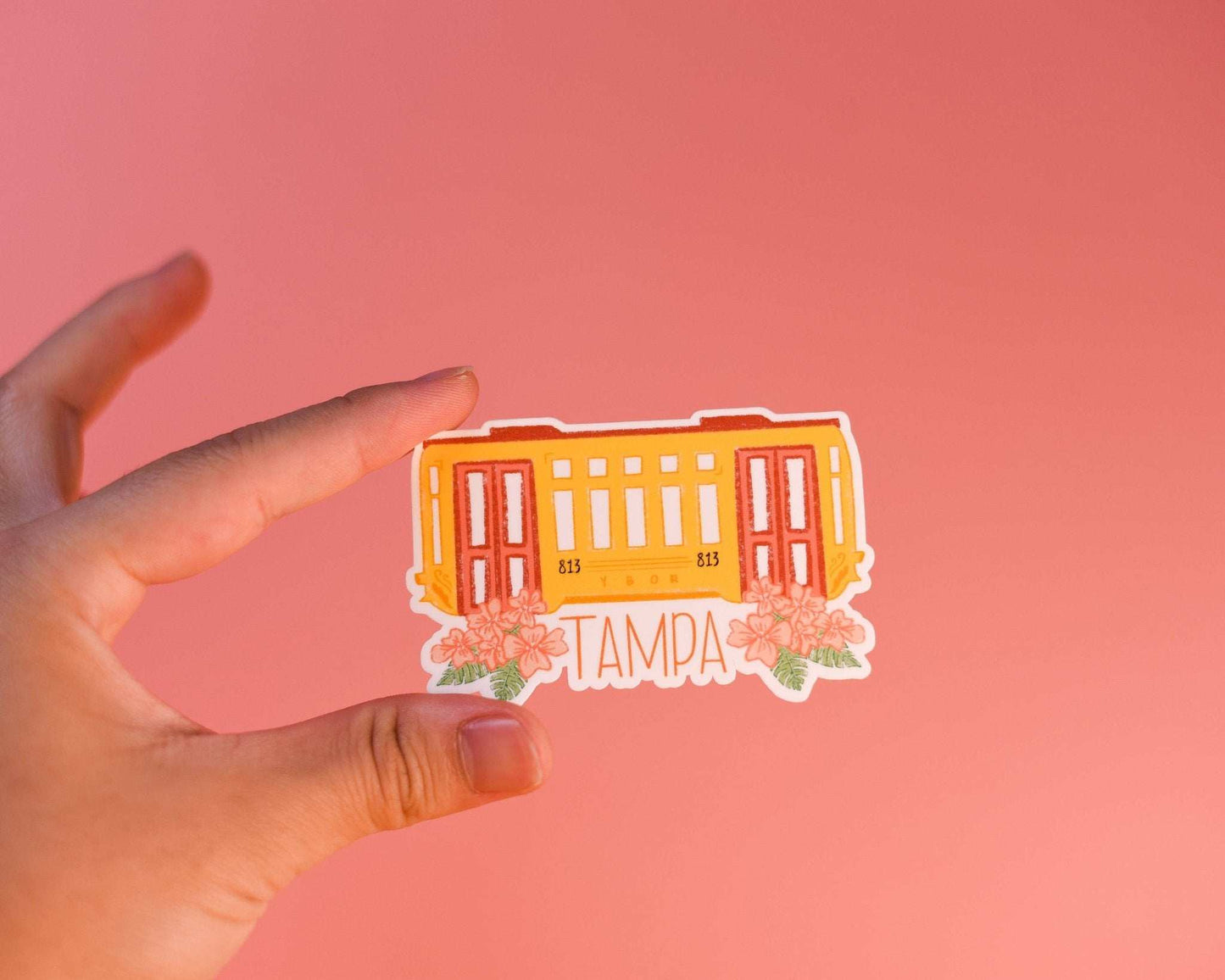 Tampa Trolly Sticker held against a pink background, ideal for laptops and journals.