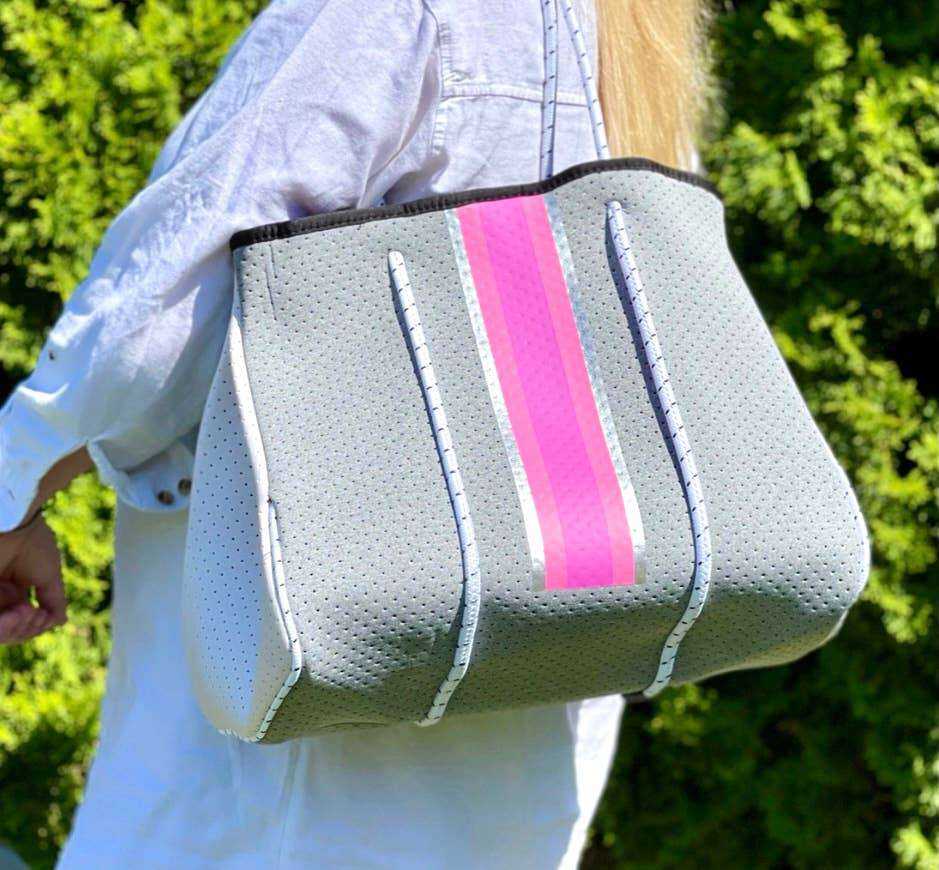 The Aniella Neoprene Tote in gray with pink stripe carried outdoors.