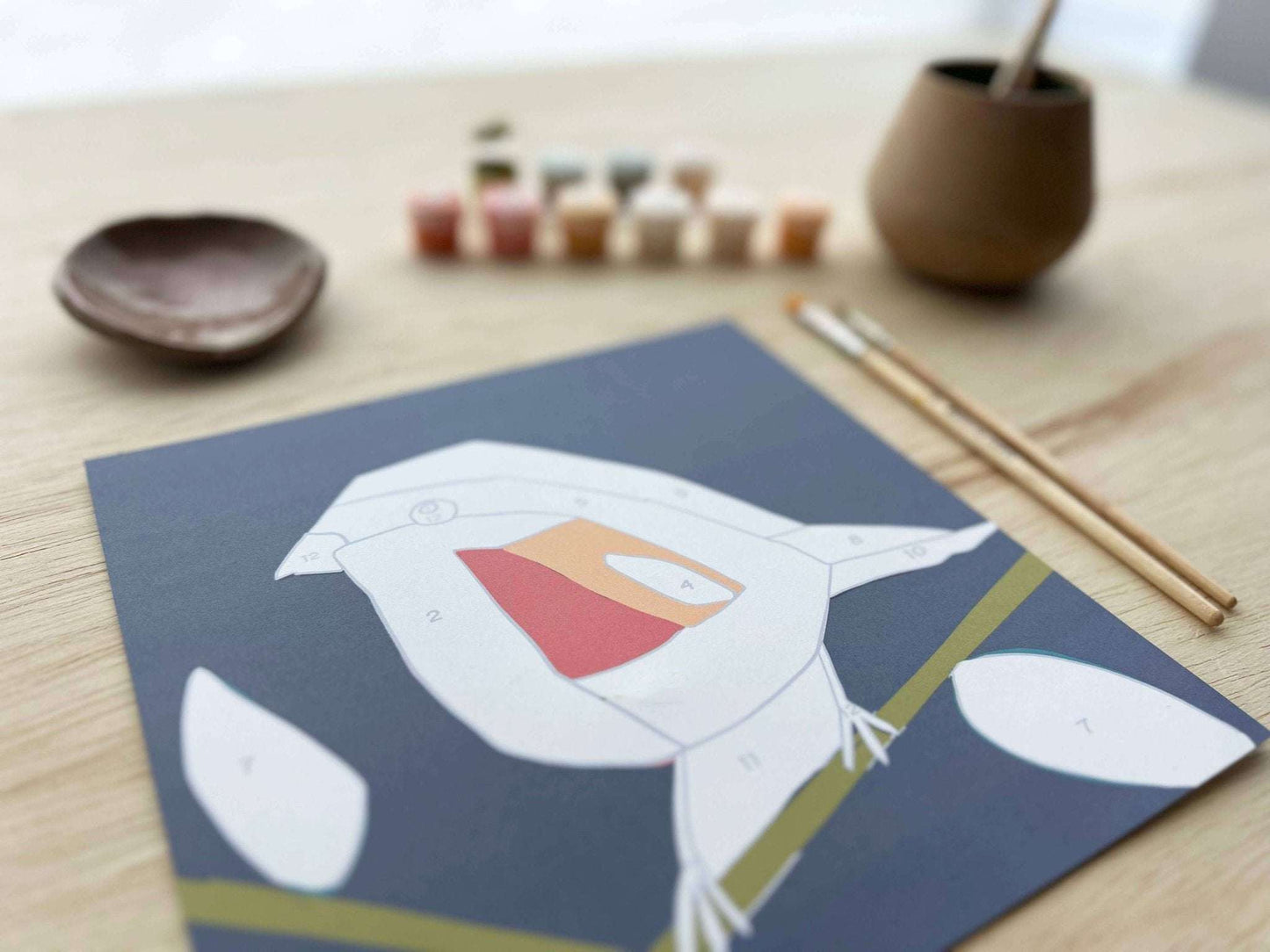 Paint by Number Kit with bird-themed canvas and art supplies on a wooden table.