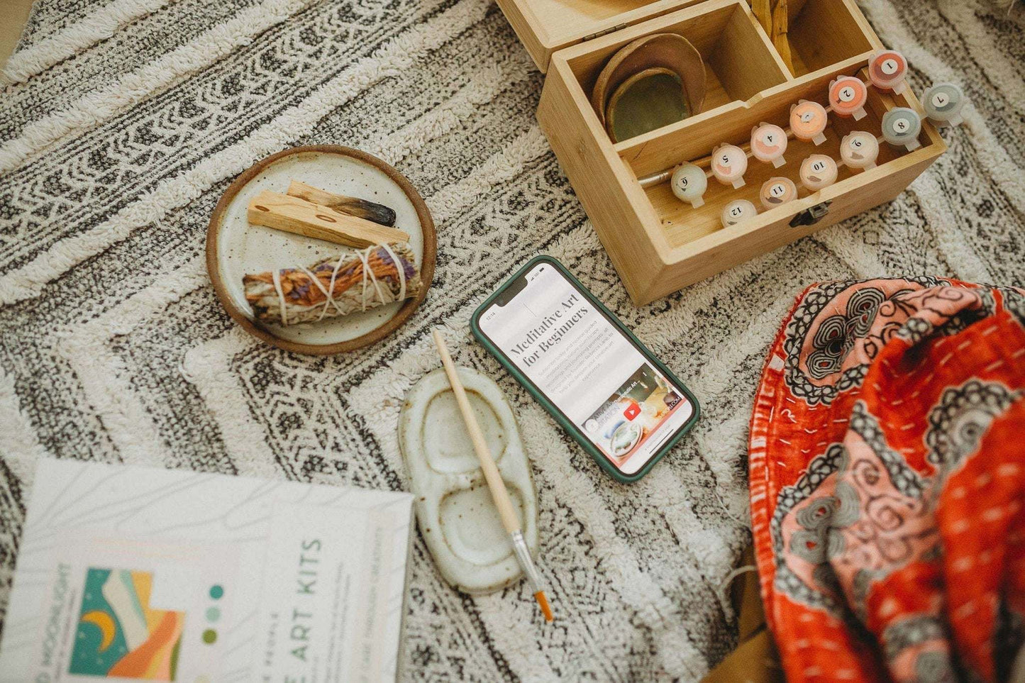 Paint by Number Kit with easel, brushes, paints, and meditation guide on patterned fabric.
