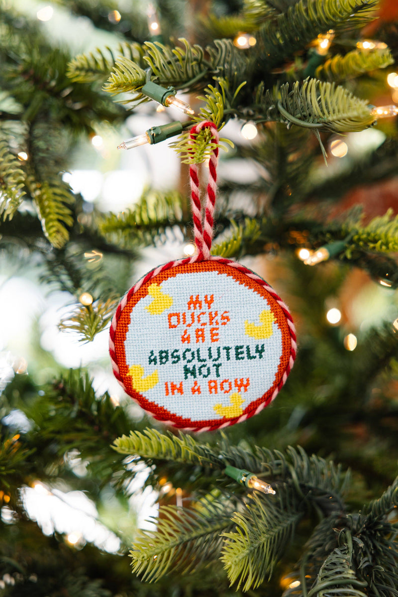 Needlepoint ornament ducks in a row hanging on a Christmas tree with festive lights.