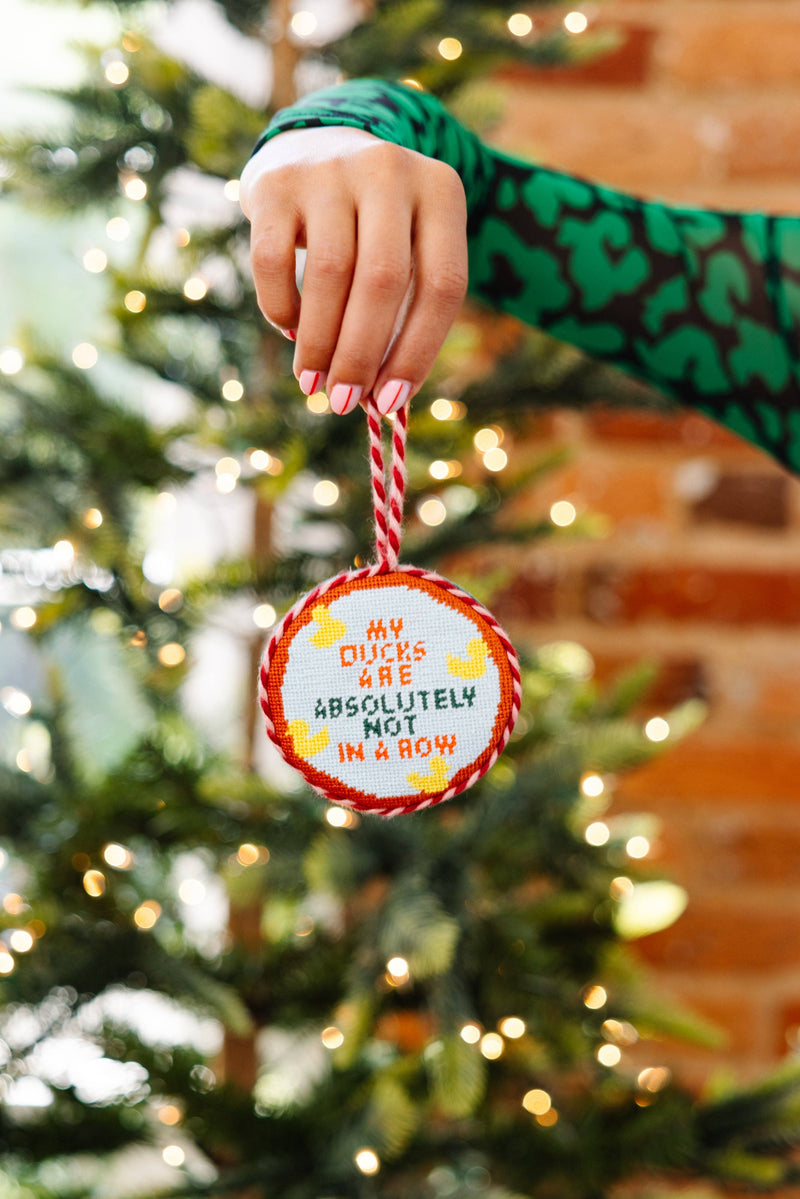 Needlepoint ornament ducks in a row, hanging from a hand, festive holiday decor with vibrant colors.