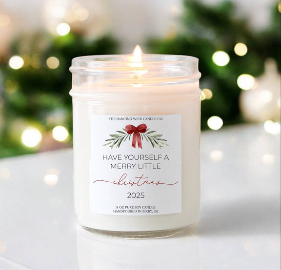 Merry Little Christmas candle with festive label and glowing flame on a blurred holiday background.
