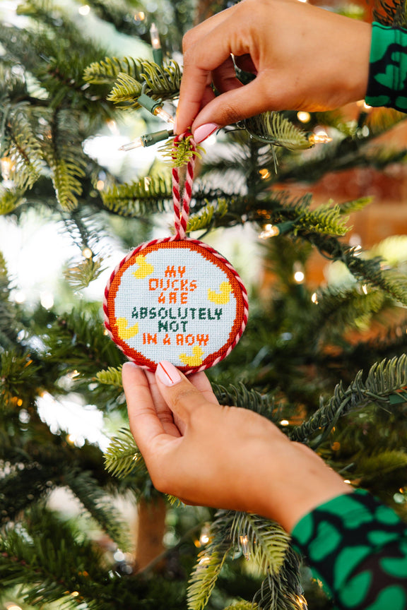 Person hanging a Furbish Studio needlepoint ornament ducks in a row on a Christmas tree.