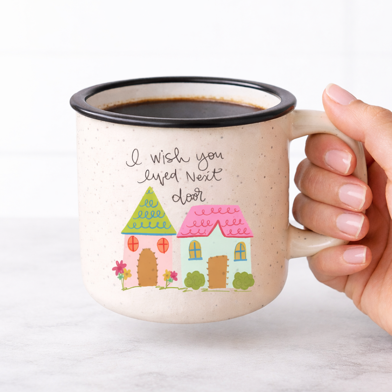 Mug with house design and text held by a hand on a white background