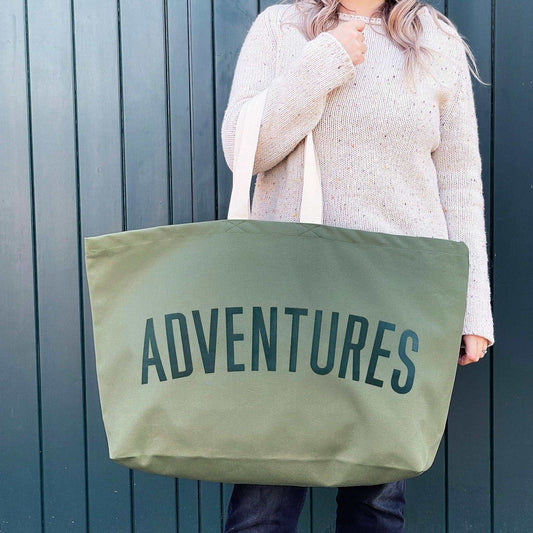 Olive green oversized canvas bag with "Adventures" printed, designed for travel and outdoor use.