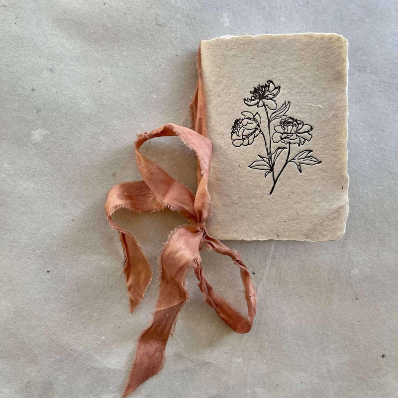 Artisan-made small notebook with floral paper cover and silk ribbon.
