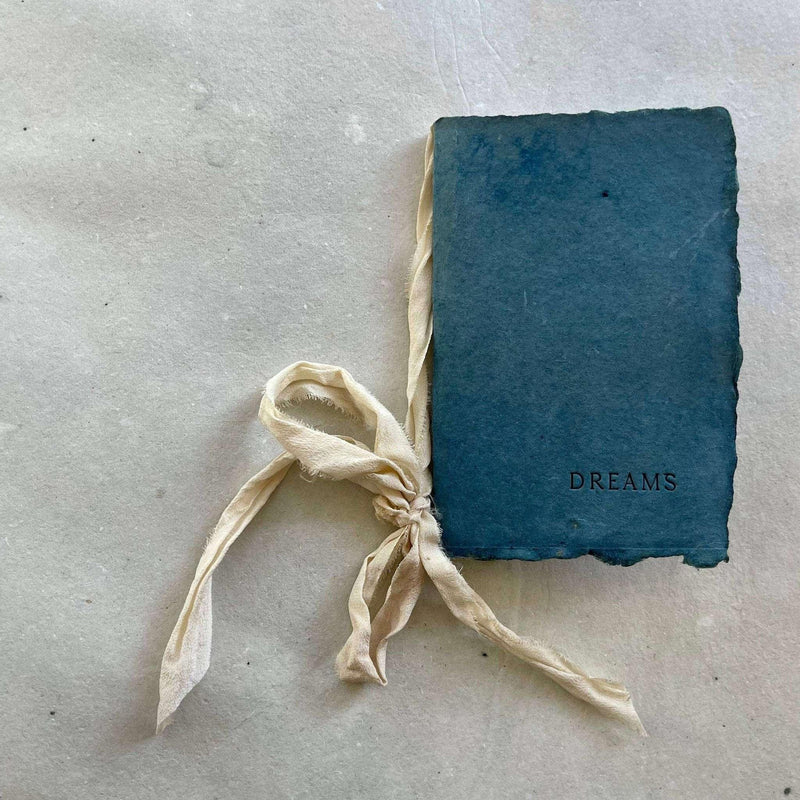Artisan-made small notebook with blue cover, labeled "Dreams" and tied with a silk ribbon.