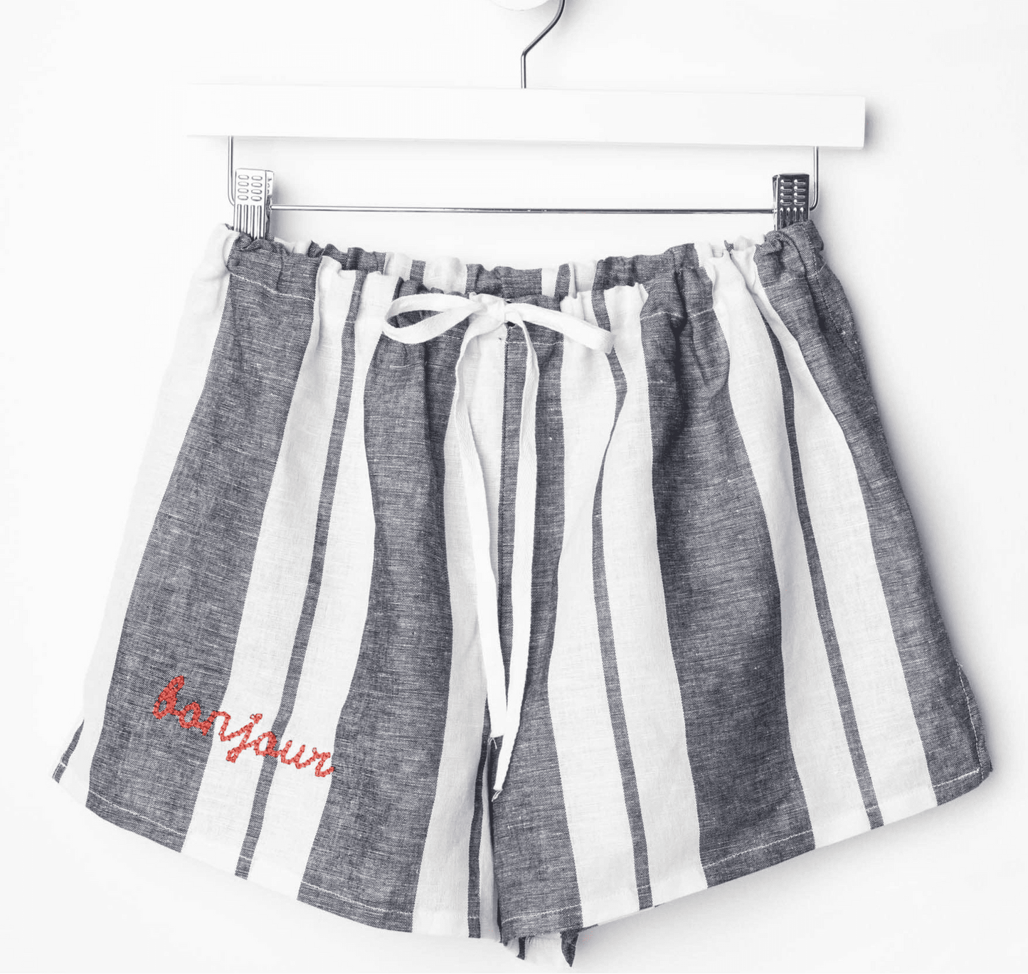 Linen PJ shorts with elastic waist and ribbon drawstring, featuring striped pattern and "Bonjour" text on the hem.