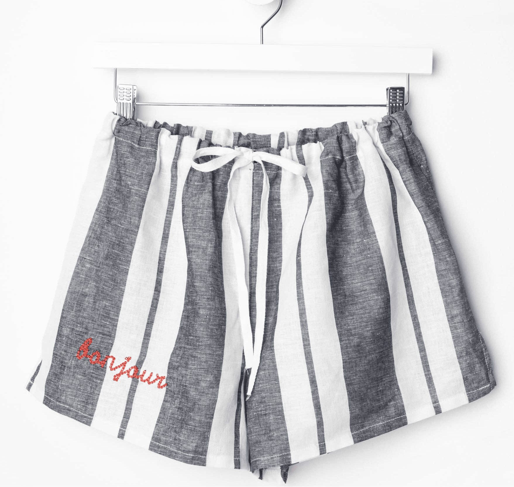 Linen PJ shorts with elastic waist and ribbon drawstring, featuring striped pattern and "Bonjour" text on the hem.