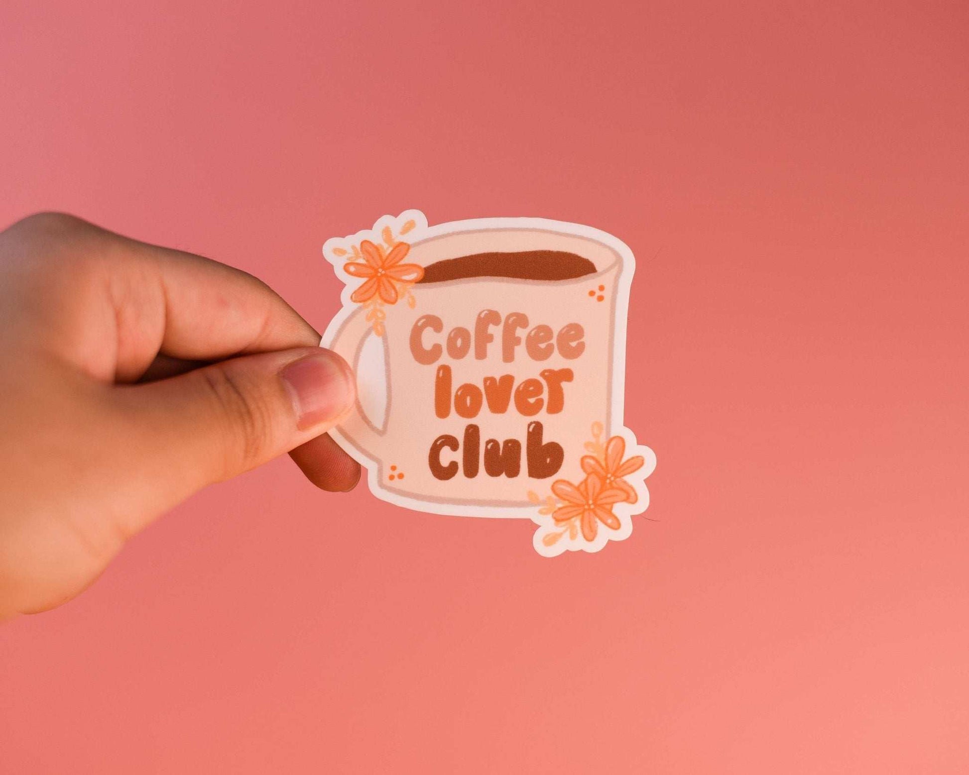 Cute coffee sticker held by hand with a pink background.