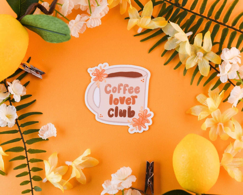 Coffee sticker featuring a mug with "Coffee lover club" text, surrounded by flowers on an orange background.