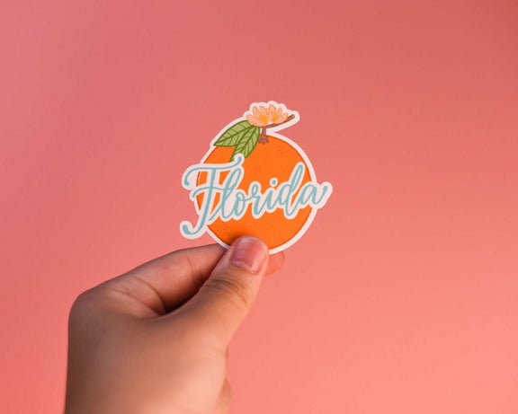 Florida Orange Sticker held against a coral background.