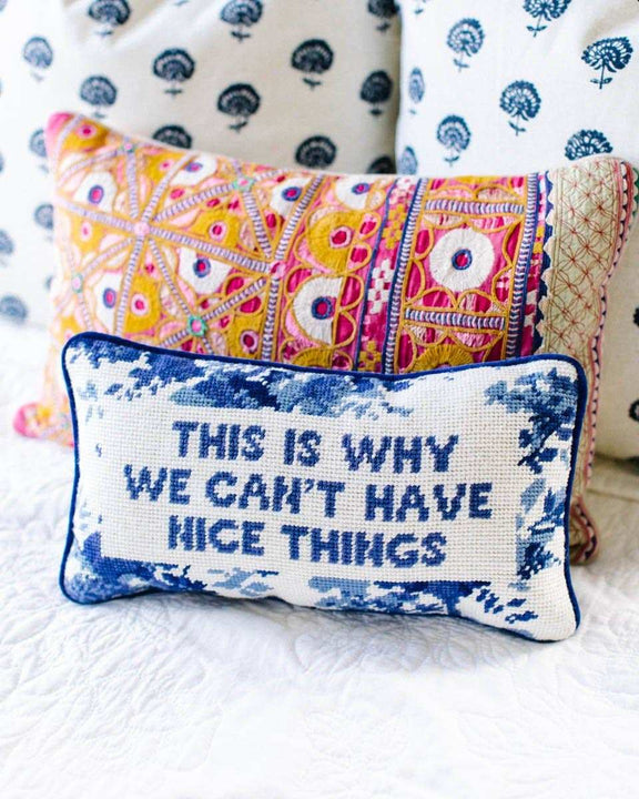 Nice Things Needlepoint Pillow with blue velvet backing on patterned sofa.