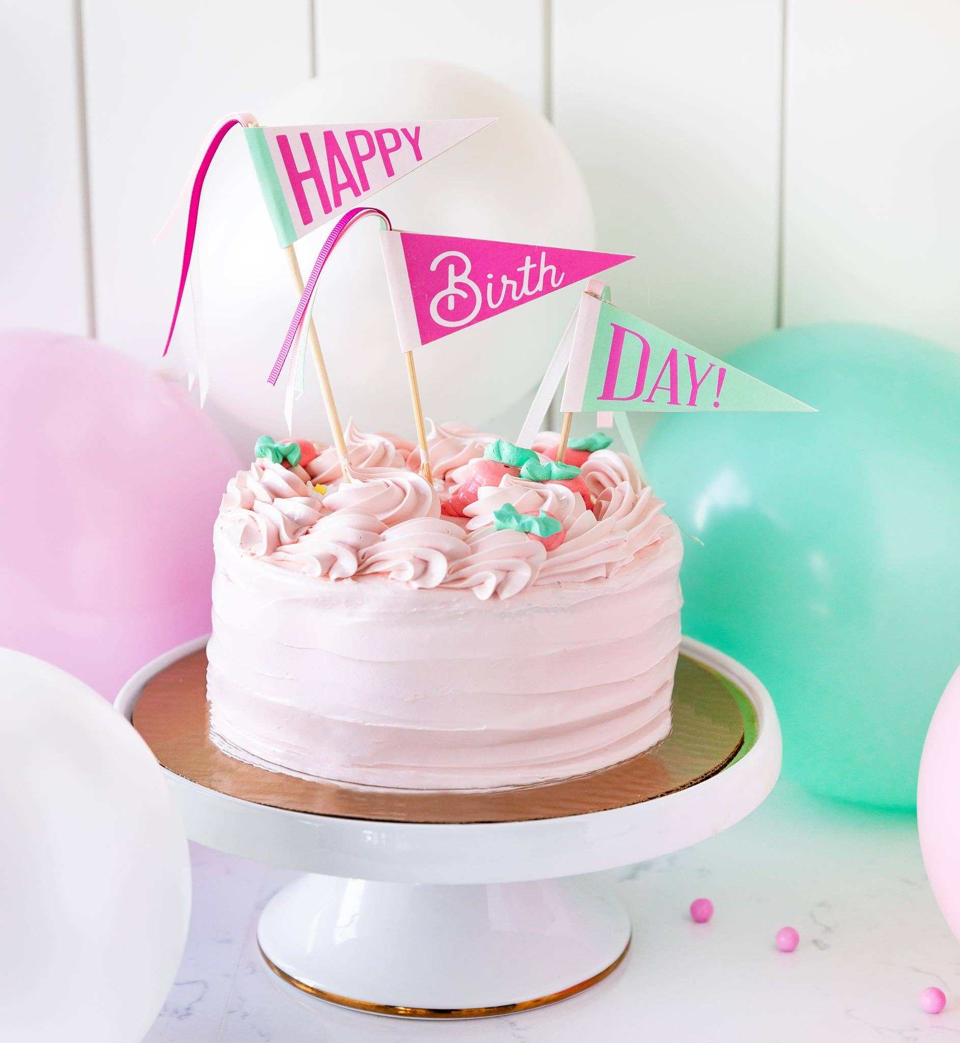 Pink happy birthday cake with pennant toppers.