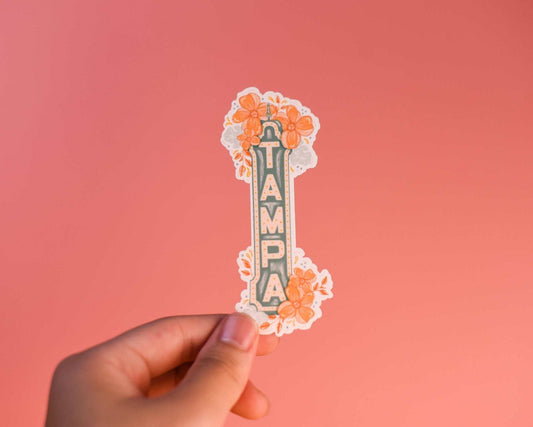 Tampa Sign Sticker with floral design held against a coral background.