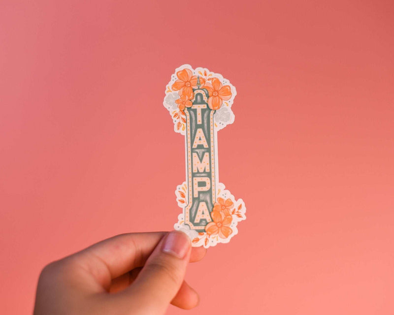 Tampa Sign Sticker with floral design held against a coral background.